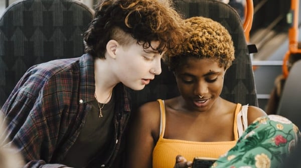 Two young women looking at a phone on a bus