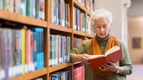 Woman reading a book next to a bookcase